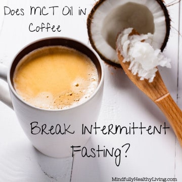 A white coffee mug with frothy coffee in it ontop of a white wood table next to a wooden spoon with MCT containing coconut oil in it. Next to the spoon is half of a coconut. Text overlay says Does MCT oil in coffee break intermittent fasting? mindfullyhealthyliving.com