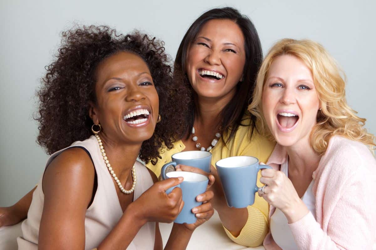 3 women laughing and smiling together while holding coffee cups