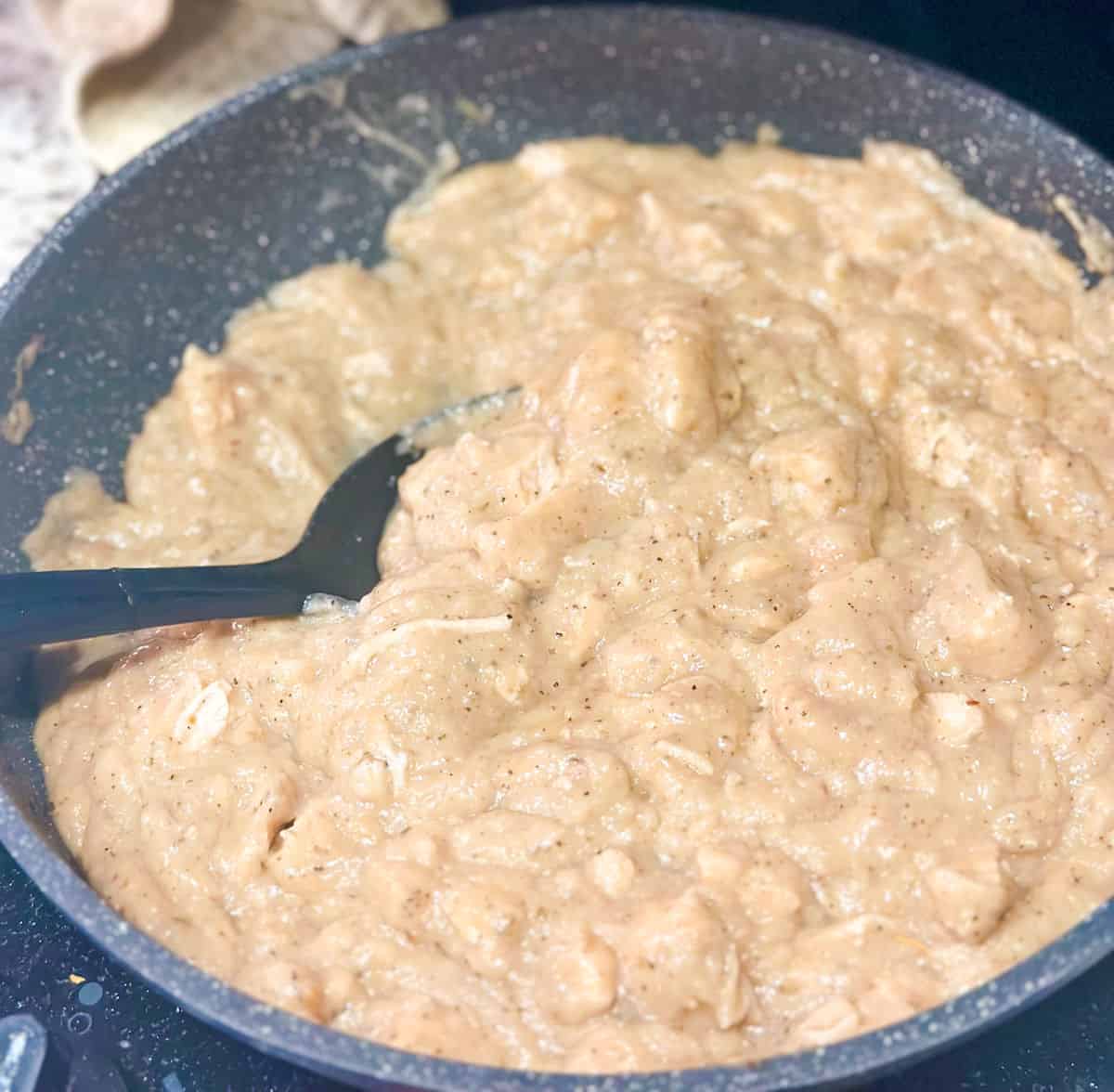 Close up photo of creamy keto alfredo sauce mixed with chunks of chicken heating in a skillet.