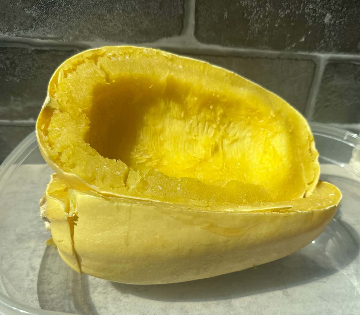 A photo of two spaghetti squash halves cooked and cooling in a clear container before being scraped.