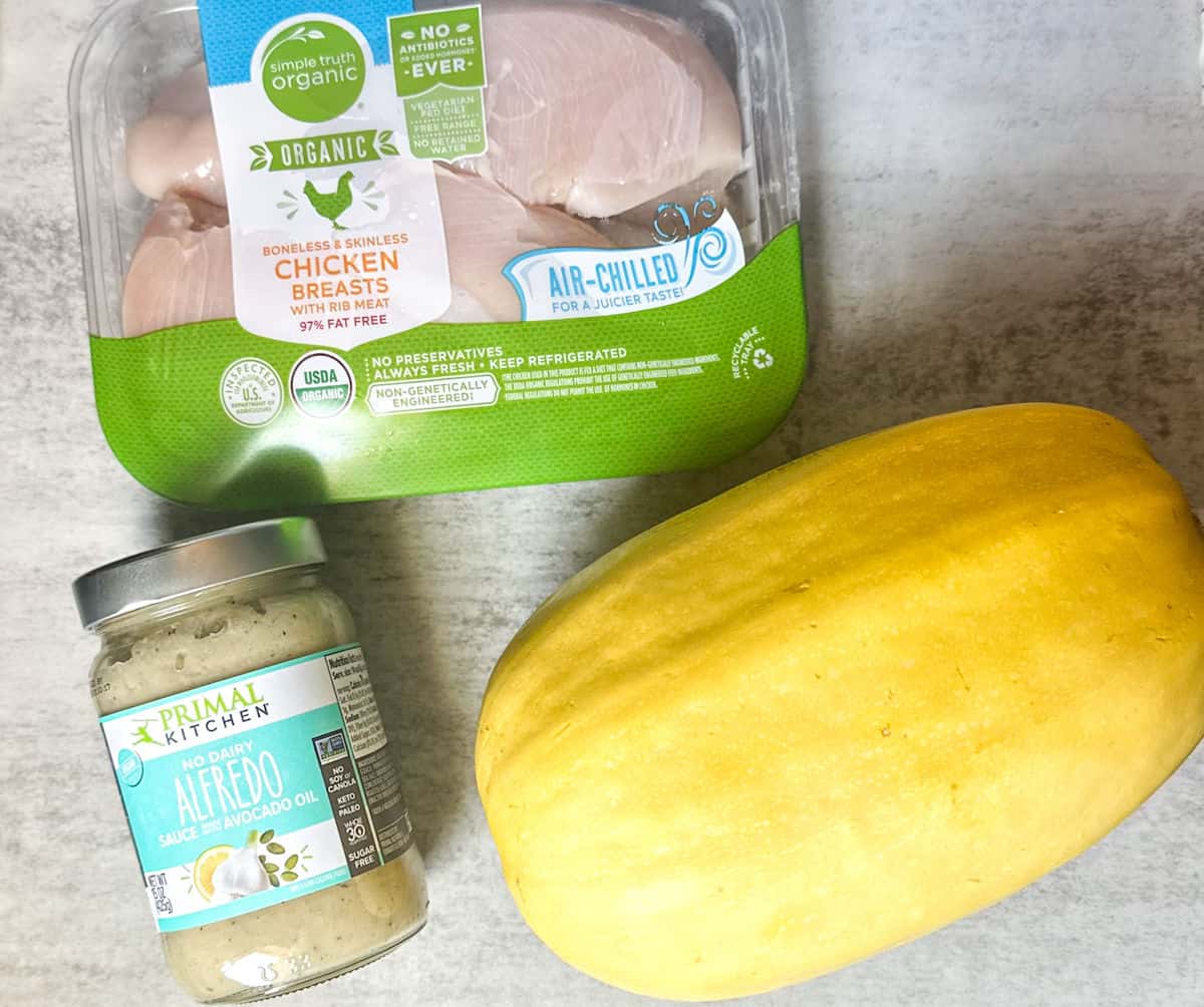 keto chicken alfredo simple ingredients photo of a whole yellow spaghetti squash, a jar of primal kitchen no dairy alfredo sauce with avocado oil, and a package of organic air chilled chicken breast.