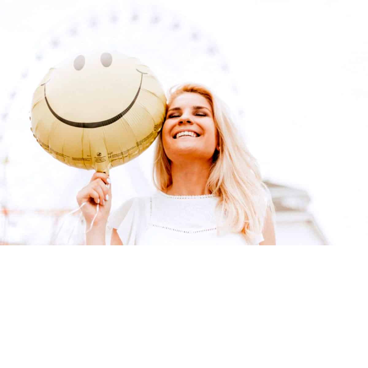 a woman smiling while holding a smiley face balloon