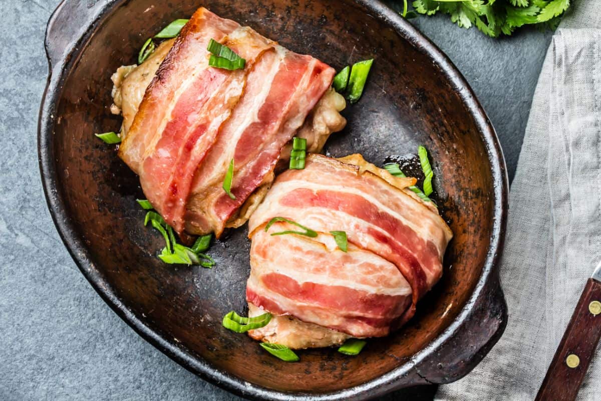 A photo of a cast iron skillet with chicken breasts wrapped in bacon and garnished with green onions.