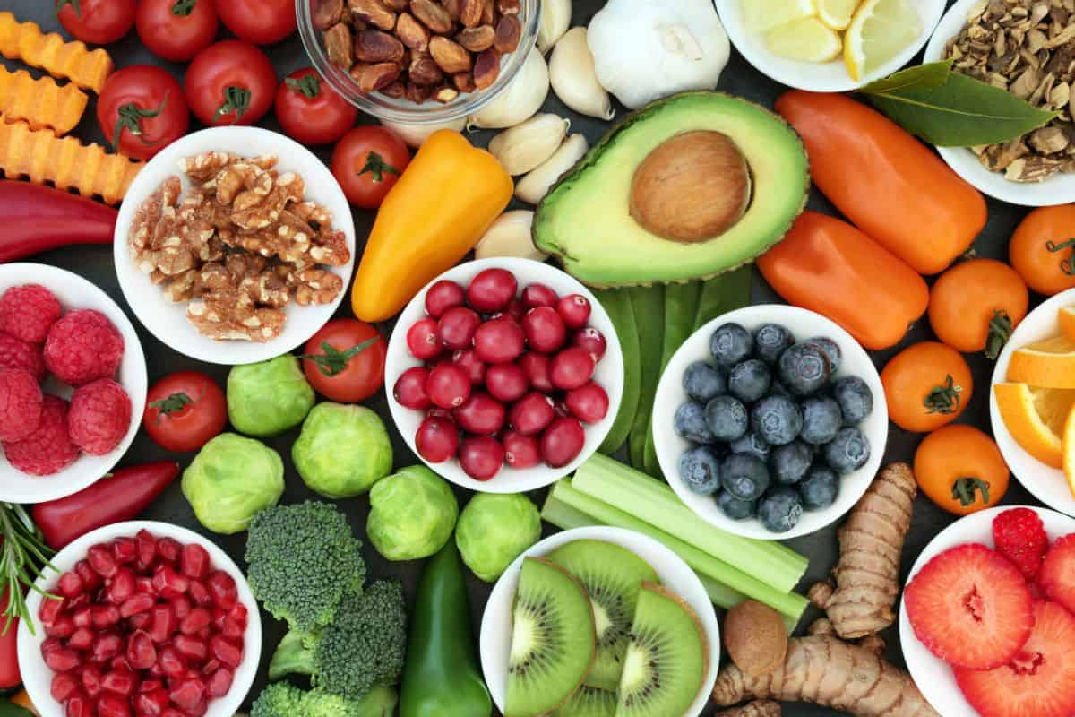 A decorative photo of many different superfoods that help heal the body and restore progesterone balance. There are berries, fruits, vegetables, roots, nuts, seeds, and herbs or various colors.