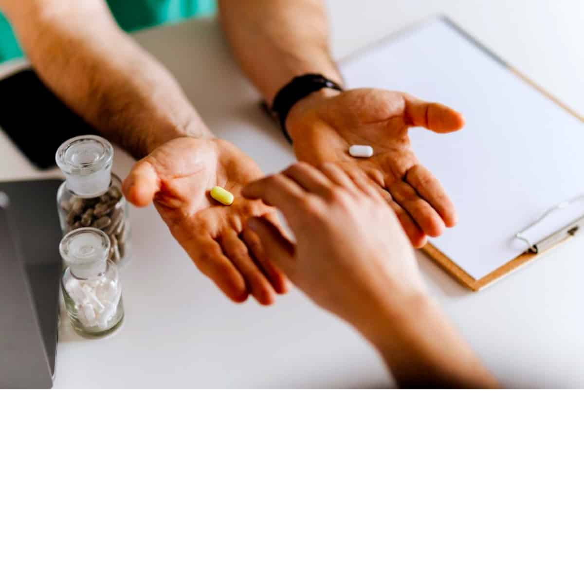 a picture of a hand with probiotic supplement in pill form being handed by a health practitioner