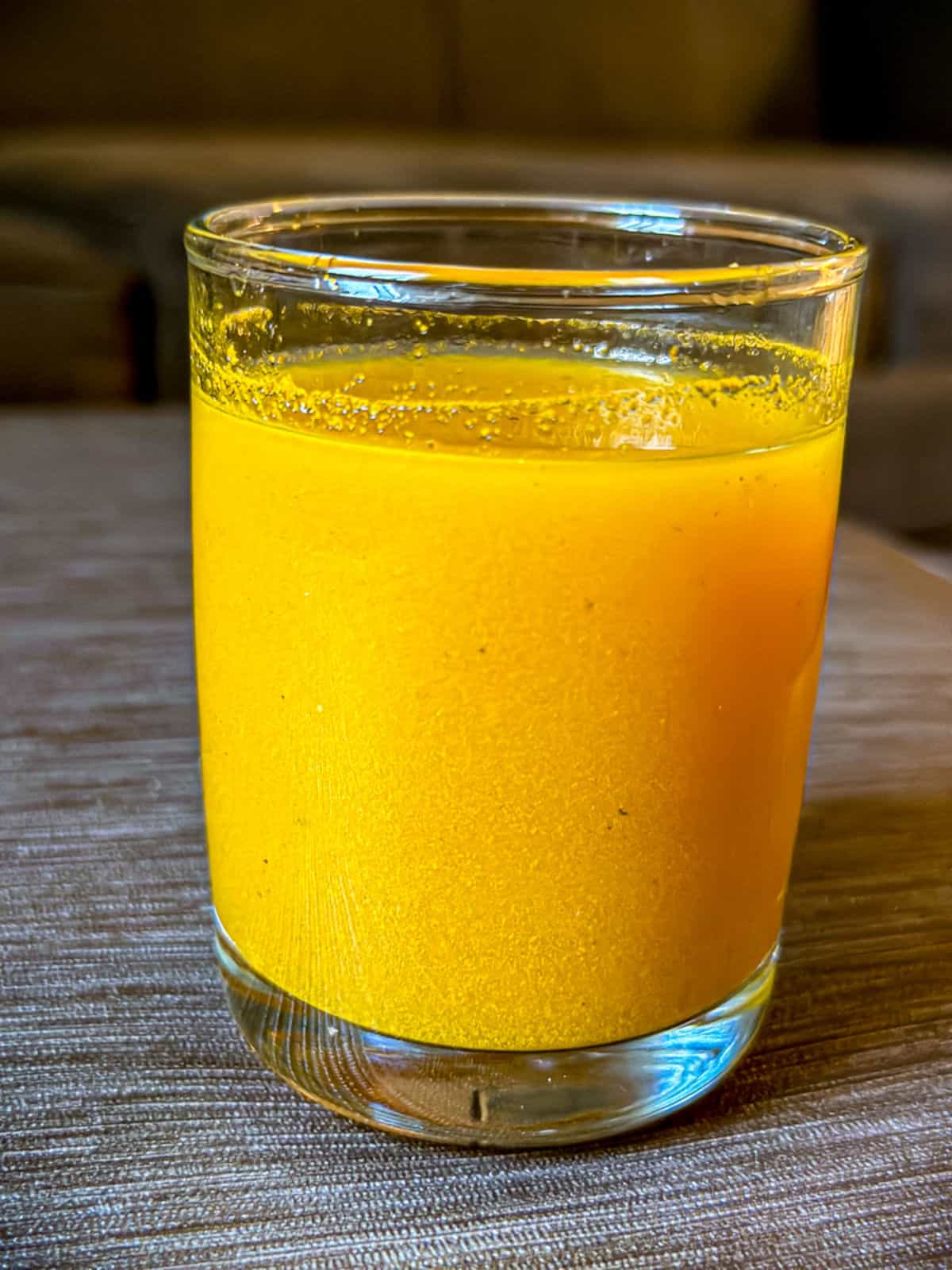 An up close photo of turmeric lemon juice made in a glass cup. There is particles showing in the mixture that shows the ingredients of turmeric, cayenne pepper, and black pepper all mixed with water.