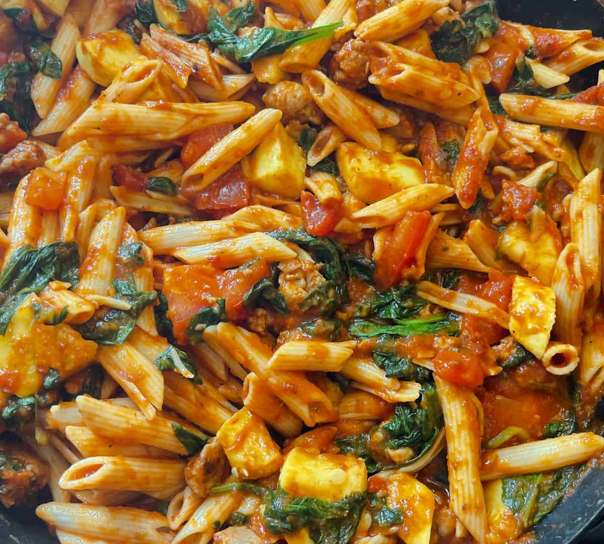 penne pasta added to sausage marinara and vegetables skillet mixed together