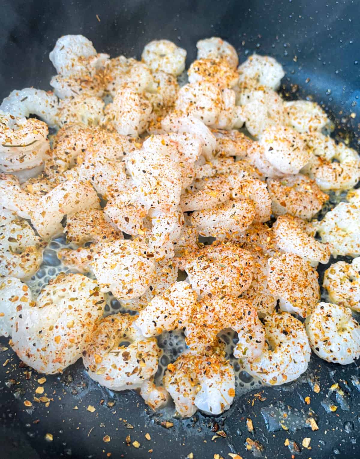 shrimp seasoned with cajun spices in a pan with oil in it