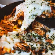 up close picture of cooked healthy spinach and sausage skillet with penne pasta and garnished with basil flakes. a spatula is taking a serving with melted mozzarella stretching away from the skillet meal