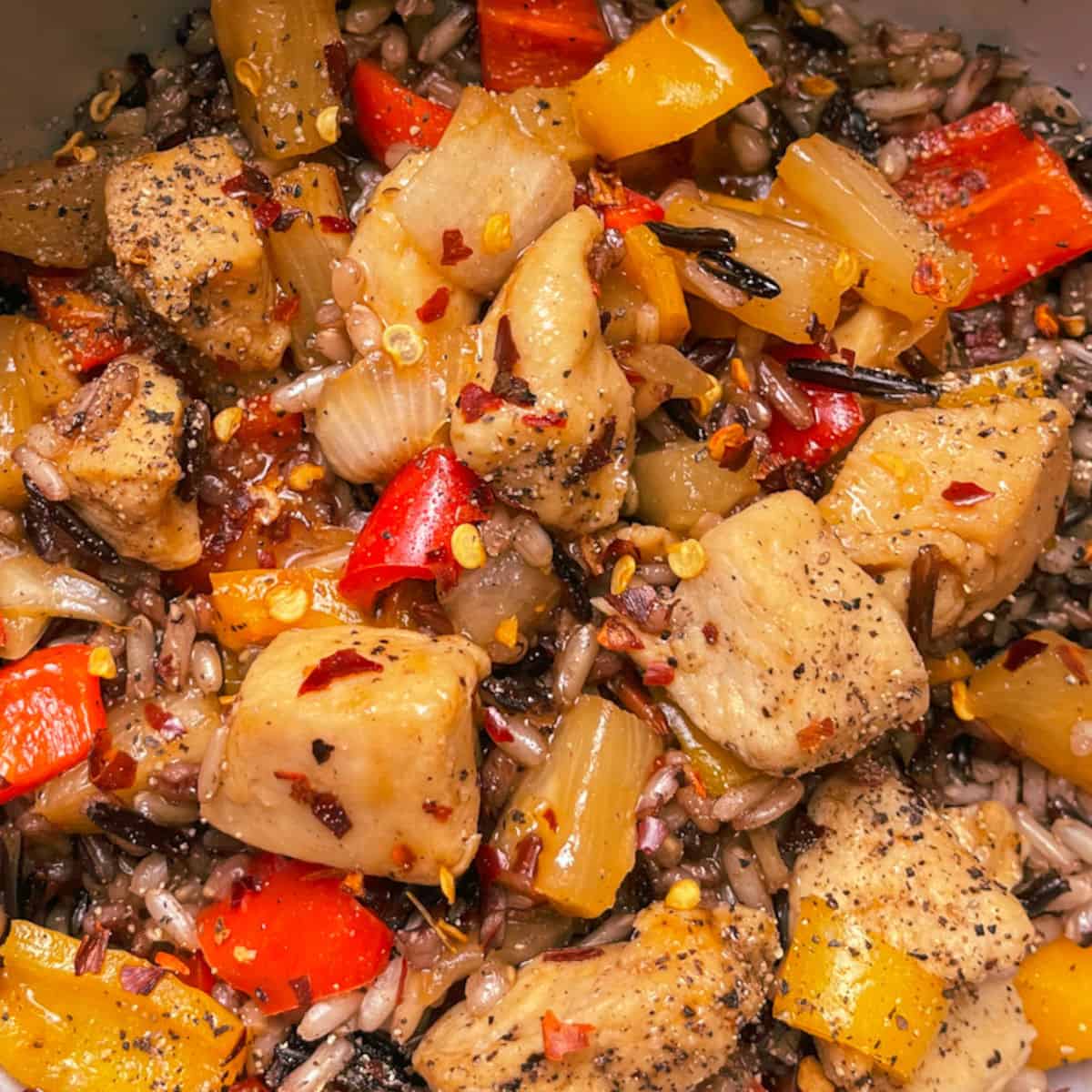 Easy Hawaiian BBQ Chicken Stir Fry Bowl in an up close photo with chicken cubes, sweet red and yellow peppers, onions, and wild rice pictured garnished with red pepper flakes and black pepper