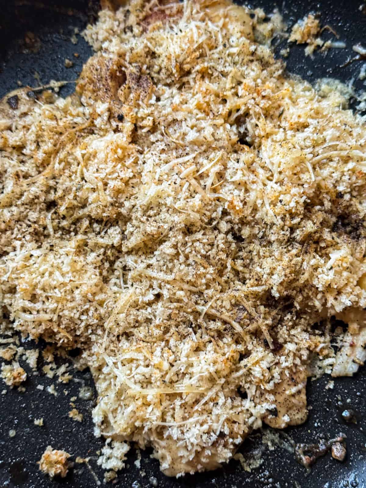 pollock fish generously covered with grated parmesan and panic seasoning mixture in a black frying pan