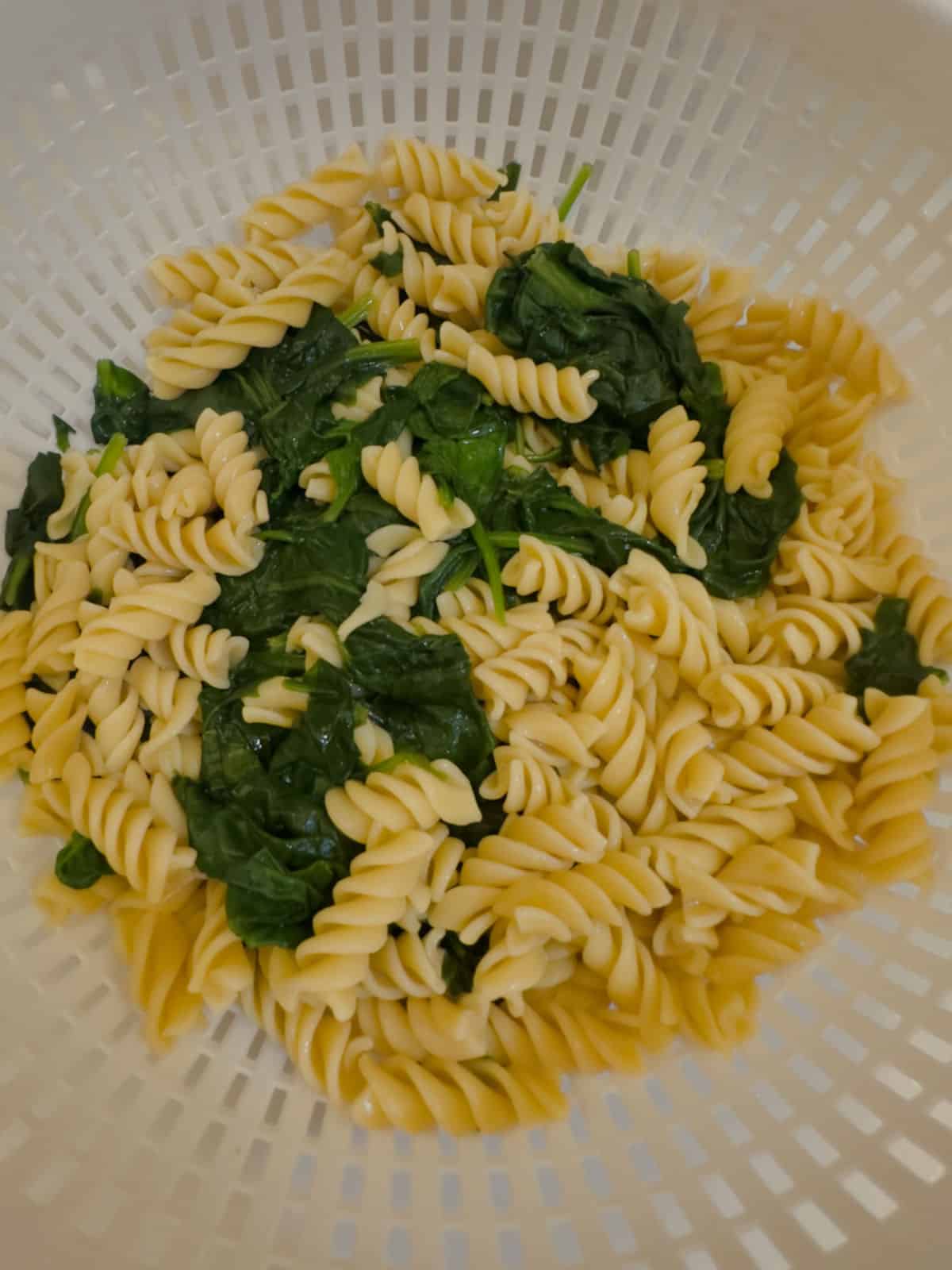 a white colander with rotini pasta and spinach