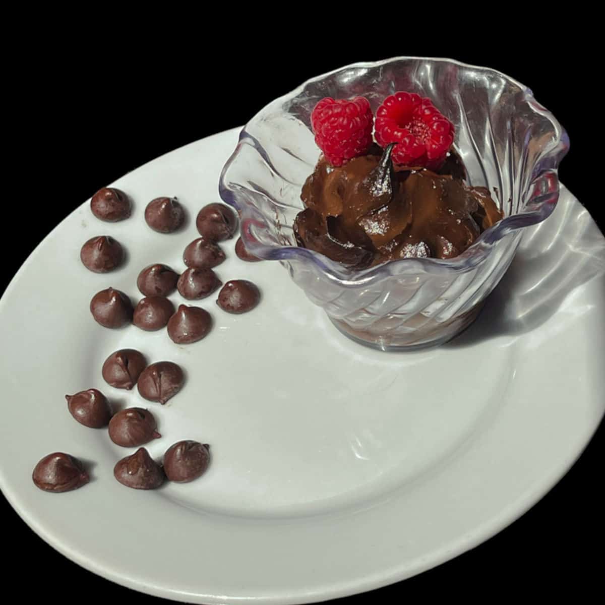 chocolate pudding I a clear decorative container on a white plate garnished with chocolate chips