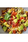 A prepared bowl of Healthy Cheesy Taco Skillet up close garnished with black pepper, tomato, avocado, cheese and a cilantro leaf