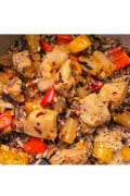 Chicken cubes cooked in BBQ sauce with red and yellow sweet peppers, pineapple and red pepper flakes with specs of black pepper all on top of wild rice blend (black and white grains of rice)