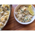 side of a pot of prepared lemon ricotta pasta next to a white bowl of creamy lemon ricotta pasta with added chicken and garnished with a lemon wedge all atop a wooden table
