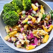a grey bowl on a blue and white placemat with broccoli, shredded jerk chicken, chopped pineapple, red onions, black beans, and cilantro on a bed of rice