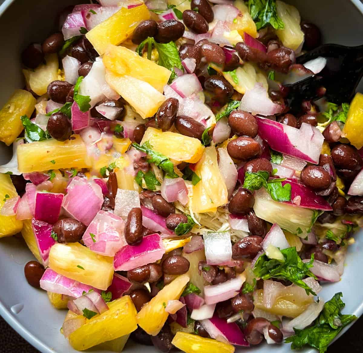 black bean and pineapple salsa in a grey bowl with chopped red onion and cilantro