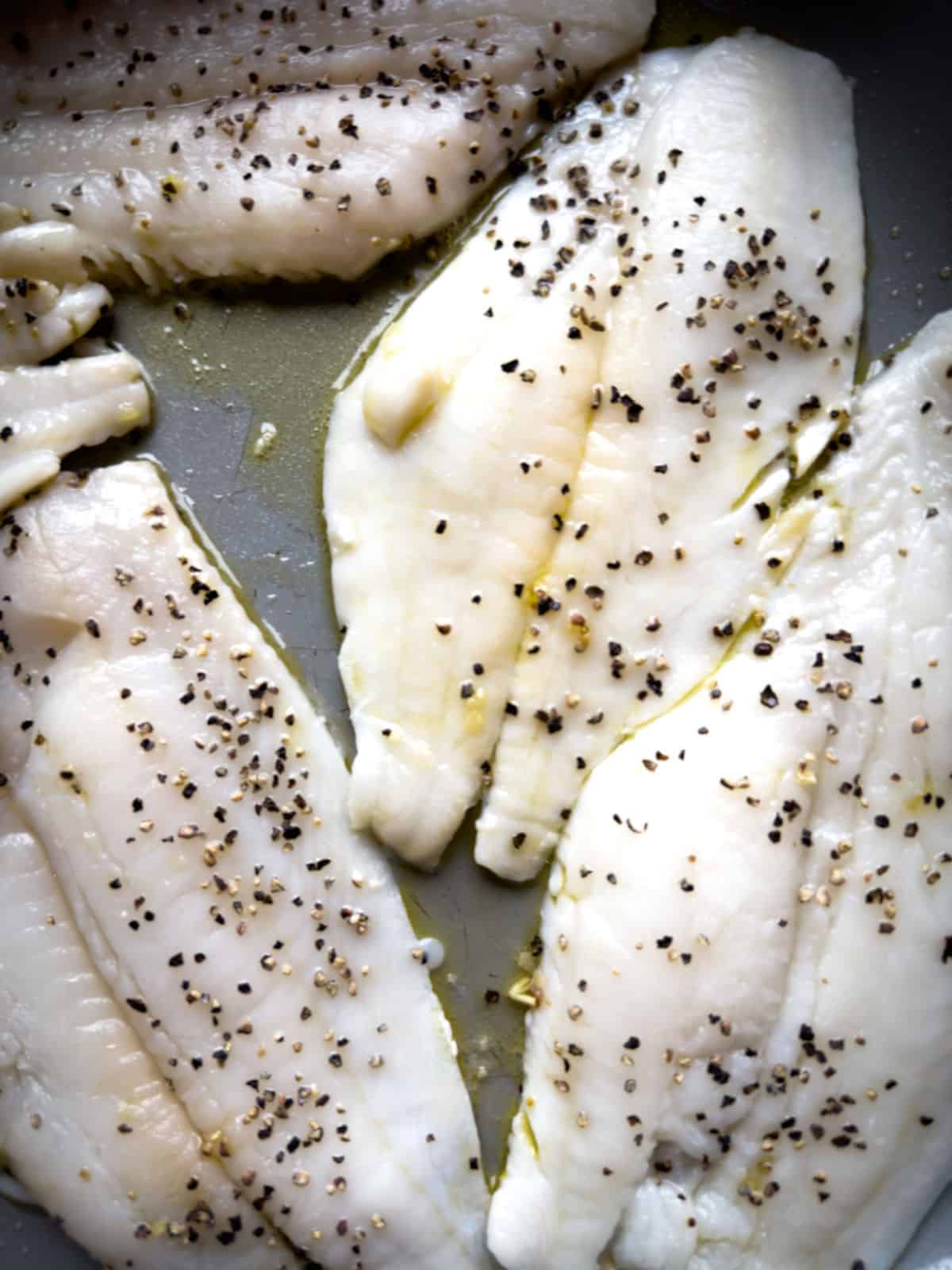 yellowtail flounder in butter sauce (ghee) seasoned with black pepper in a grey skillet, still raw