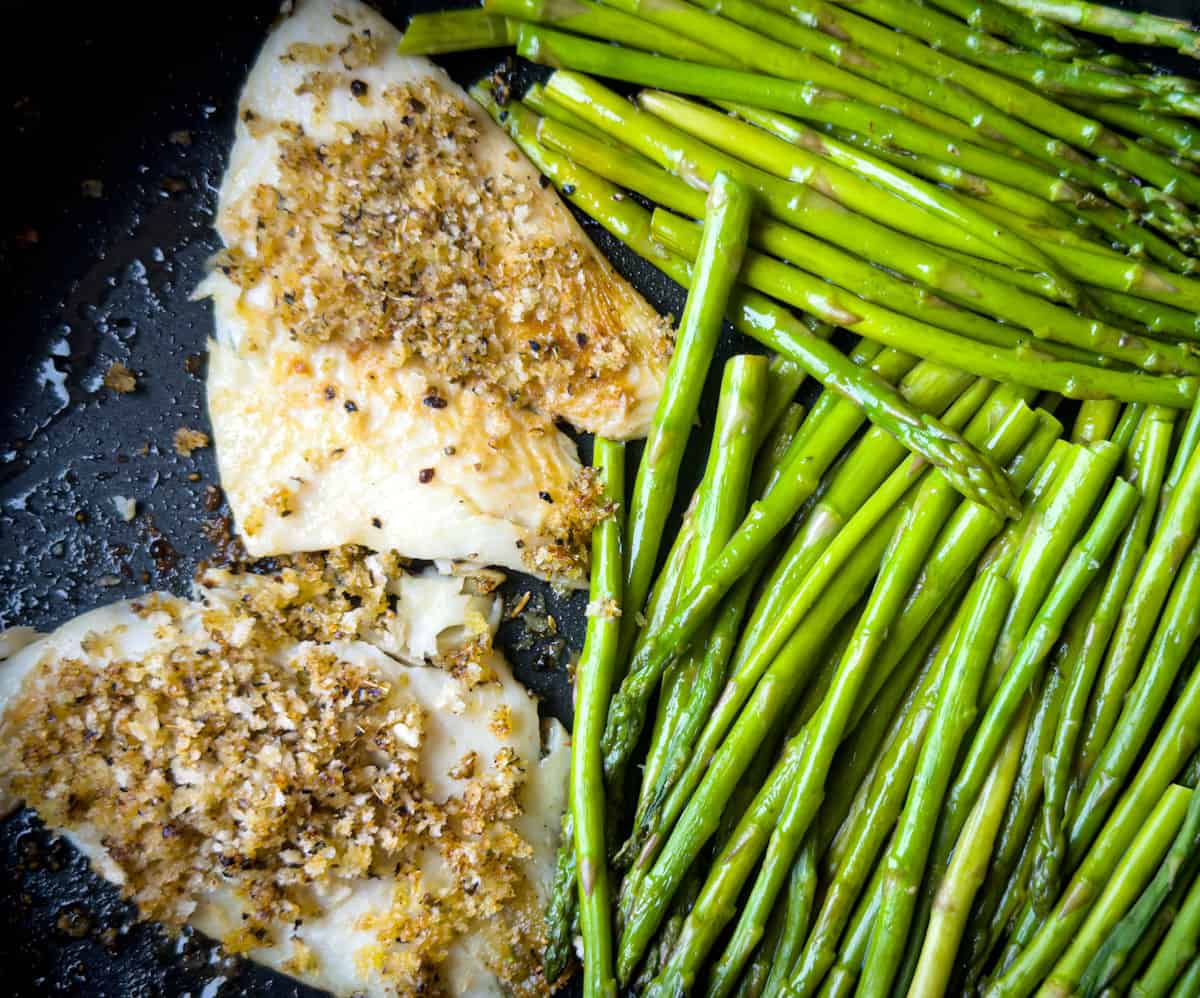 step 4 fish is done with two pieces of yellowtail flounder pictured golden spiced crust next to two handfuls of bright green asparagus in ghee cooked to perfection in a black skillet