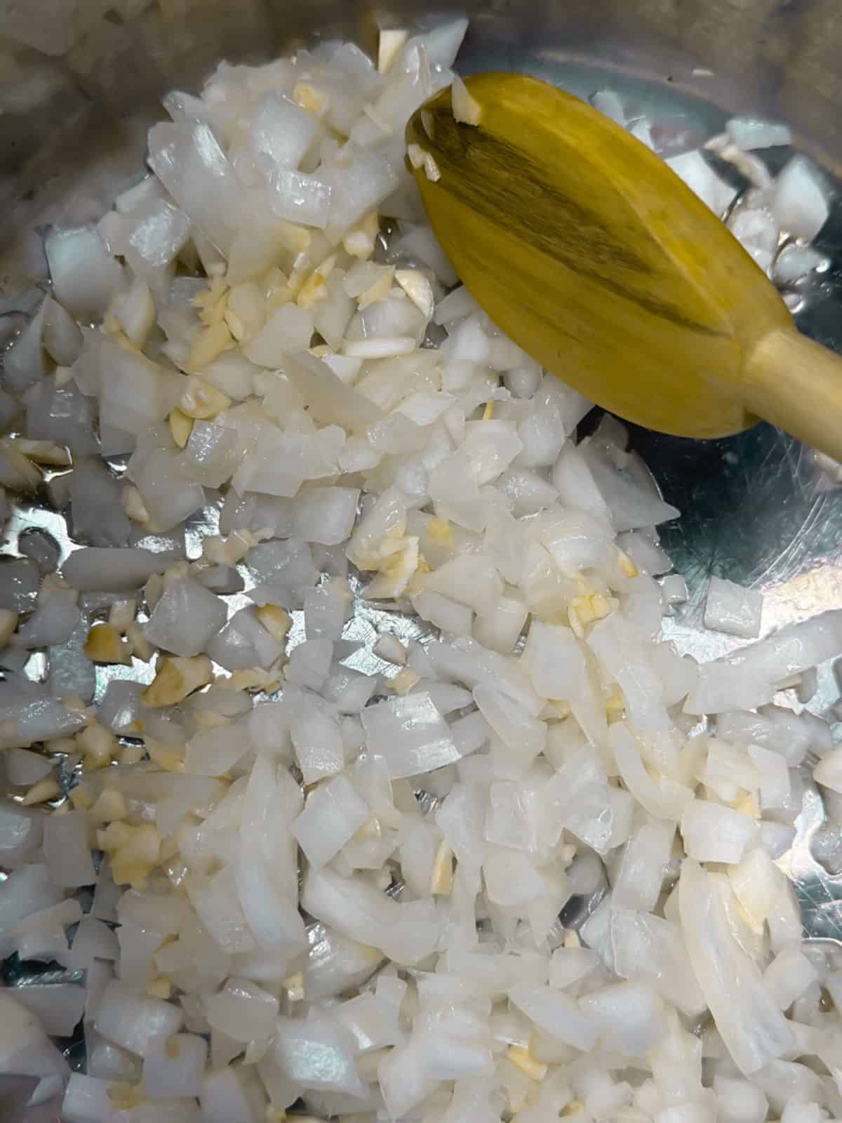the inside of an instant pot with a wooden spoon stirring chopped onions and garlic in oil