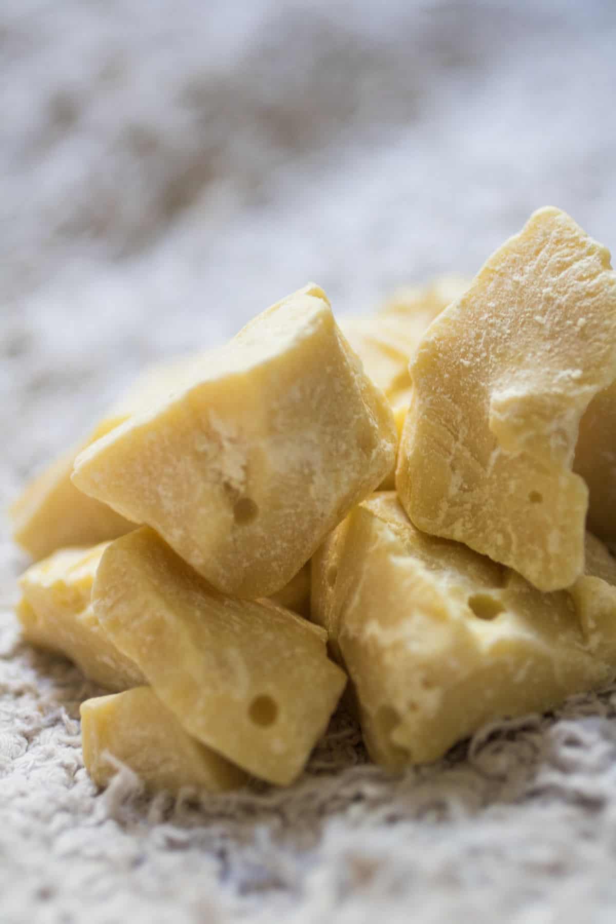 An up close picture of light yellow colored raw and hard chunks of cocoa butter on a light grey rug.