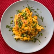 close up of a grey matte plate on a red placemat with a serving of chicken broccoli casserole garnished with green chives