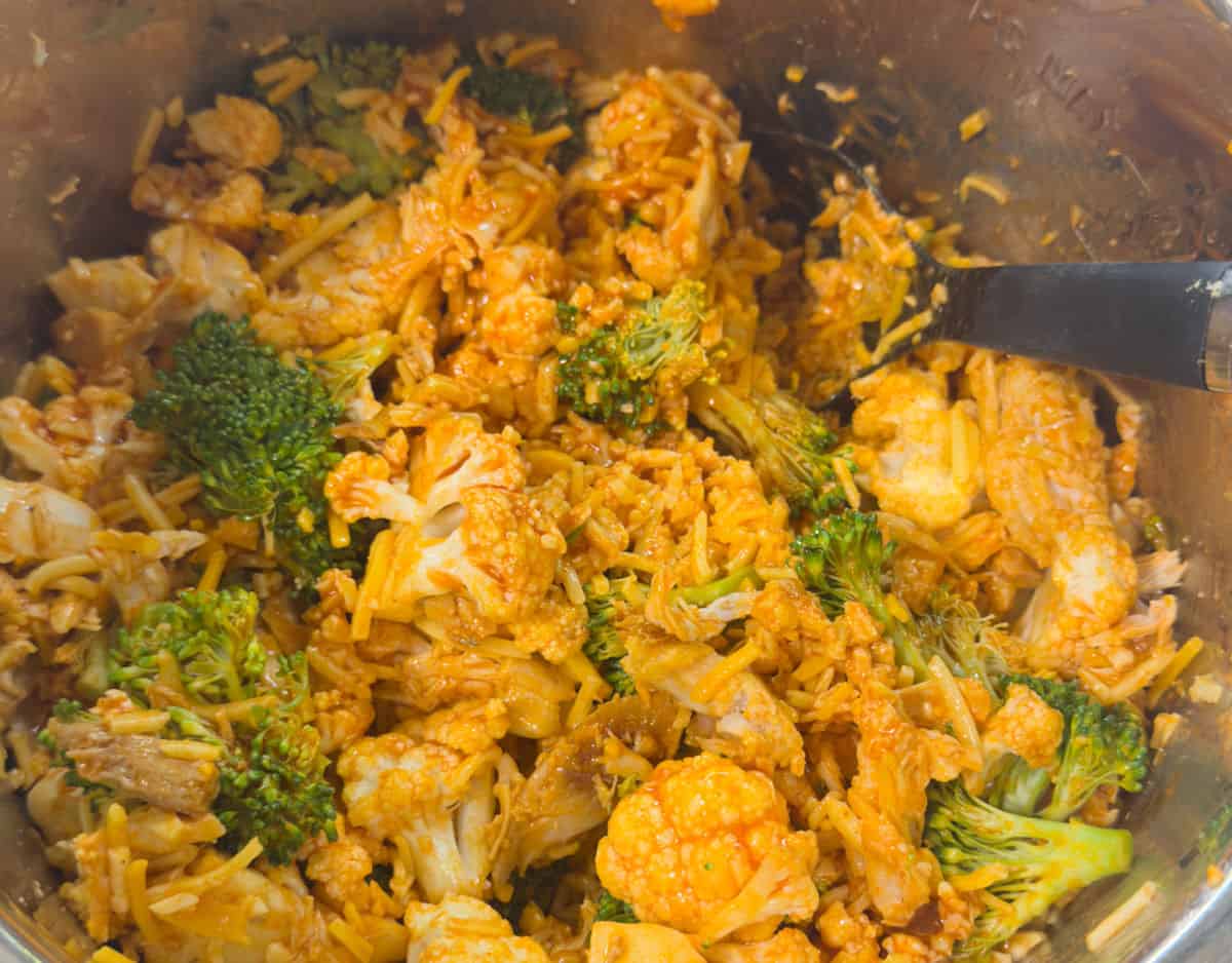 mixing fresh broccoli and cauliflower florets with shredded chicken and buffalo sauce ready to start the pressure cooking for 1 minute