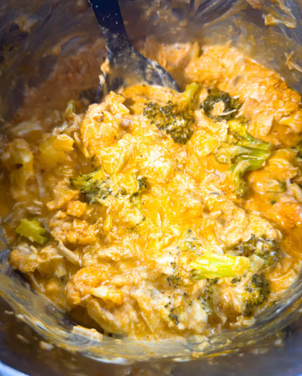 close up of the inside of instant pot silver shiny interior with chicken buffalo broccoli mixed with yogurt and cheese for a creamy finish