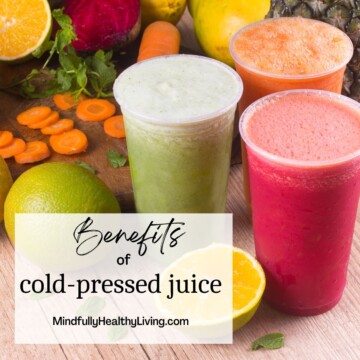 3 cups of juice, one green, one orange,and one red with slight foam at the top surrounded by cut carrots and 3 whole fruits in the background with green leaves decoratively places around. a white rectangle overlay at the bottom with black writing says, Benefits of cold-pressed juice mindfullyhealthyliving.com