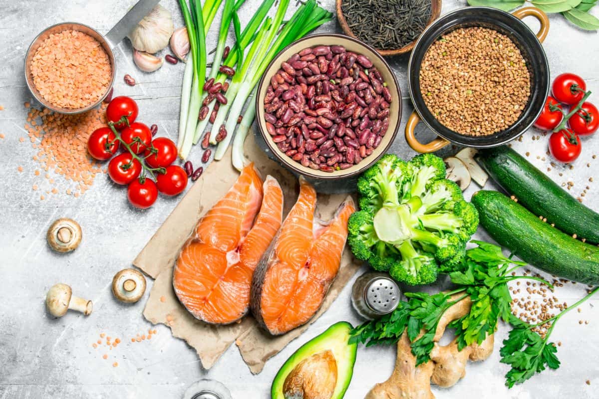a brightly colored photo of healthy foods like leeks, kidney beans, beans in a bowl, flax seeds in a bowl, spices, and herbs, salmon, avocado, ginger, parsley, broccoli, cherry tomatoes, and zucchini