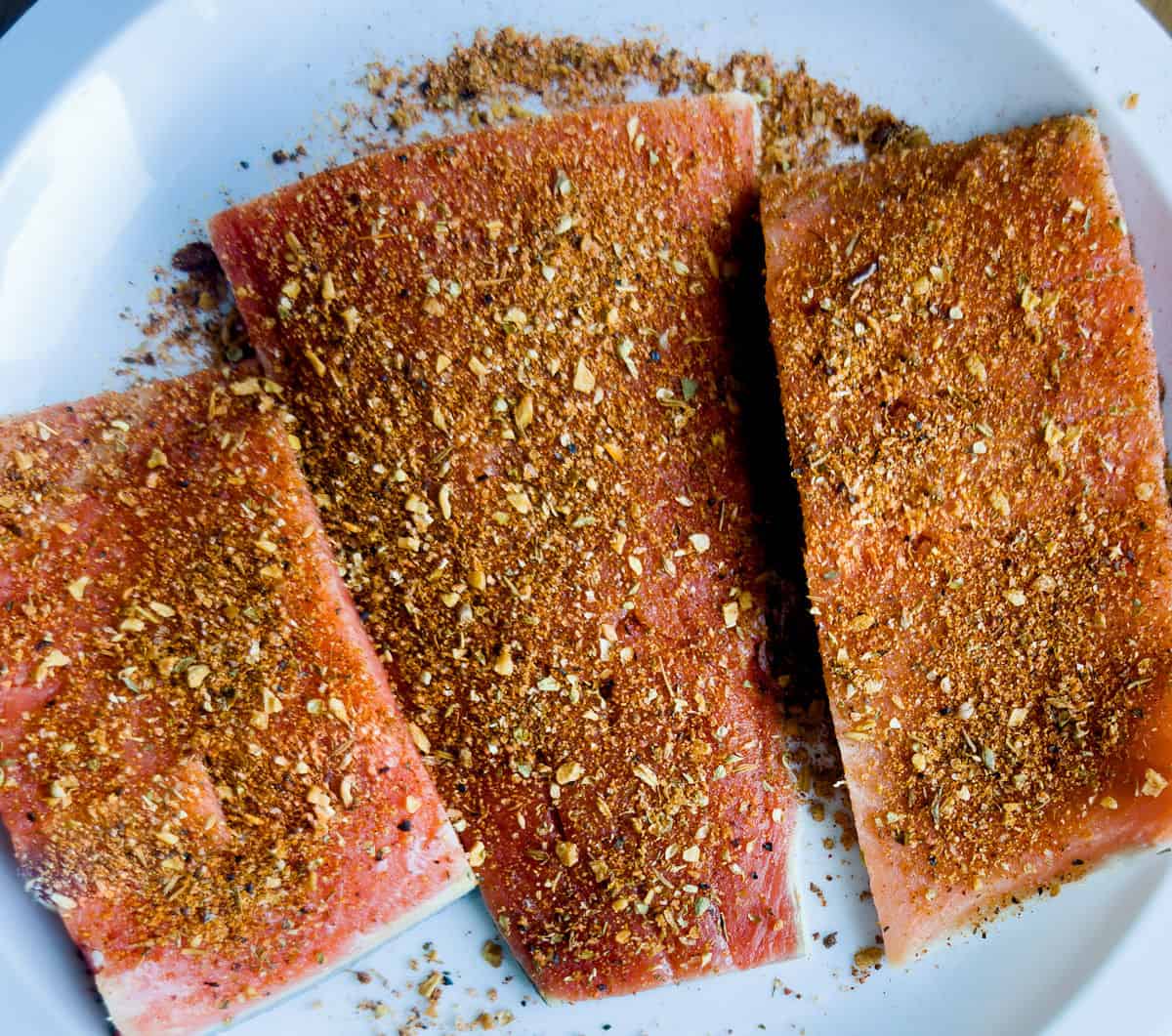 zoomed in photo of fresh salmon fillets cut and portioned into three pieces and seasoned with cajun spices on a white plate