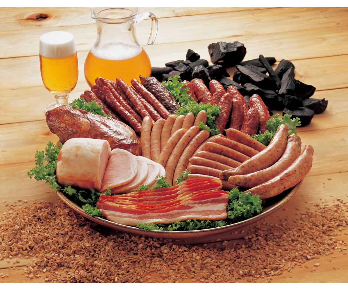 A plate filled with various types of cured meats, bacon, sausages, hot dogs, and ham garnished with lettuce leaves