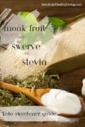 Two white transparent paint stripes with black print on top is written Monk Fruit vs Swerve vs Stevia Keto Sweetener Guide. On the top right in white print says mindfullyhealthyliving.com. all on top of a decorative photo of monk fruit powder in a wooden spoon, swerve granules in a large scoop with a green leaf on top of it, and dried stevia leaves all sitting next to sugar cubes on a wooden table.