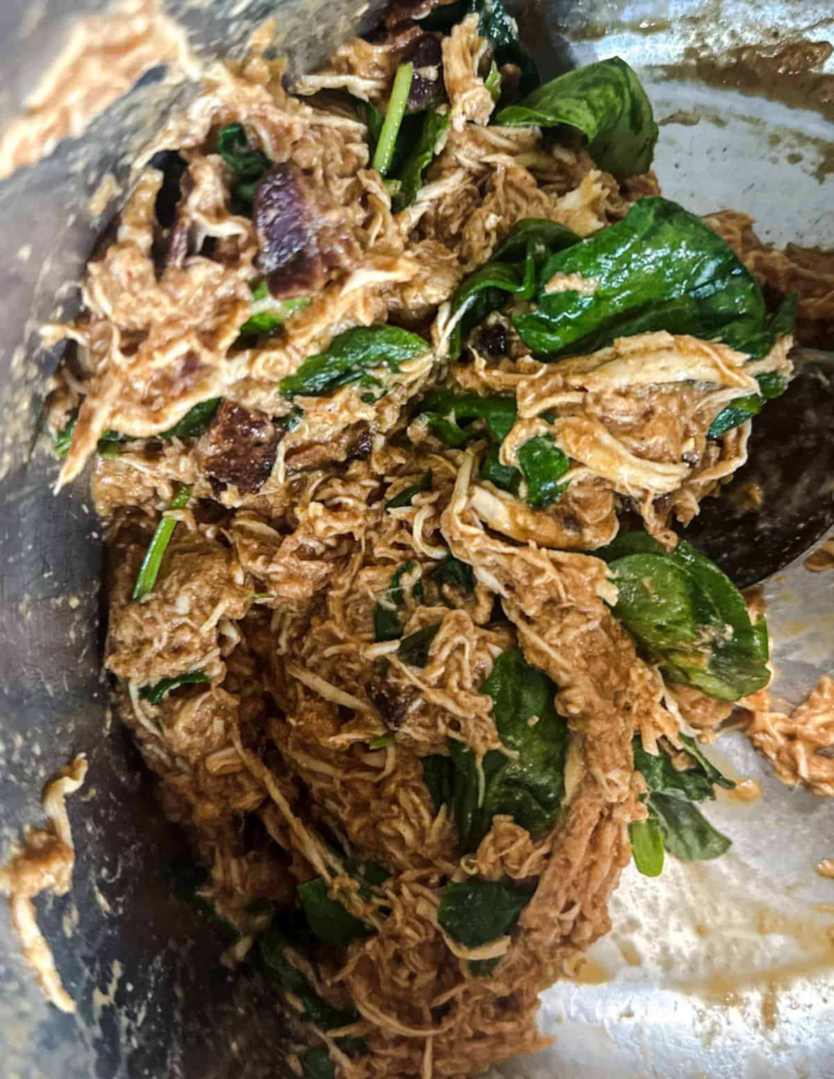 A closeup shot of the inside of an instant pot with shredded chicken mixed with BBQ sauce, yogurt, bacon bits, cheese, and spinach.