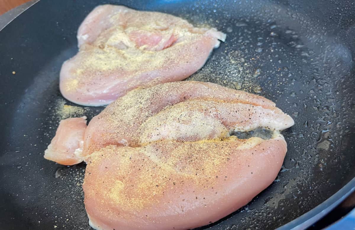 raw chicken butterfly cut and seasoned with onion and garlic powder, salt, and pepper in a skillet seasoned with oil