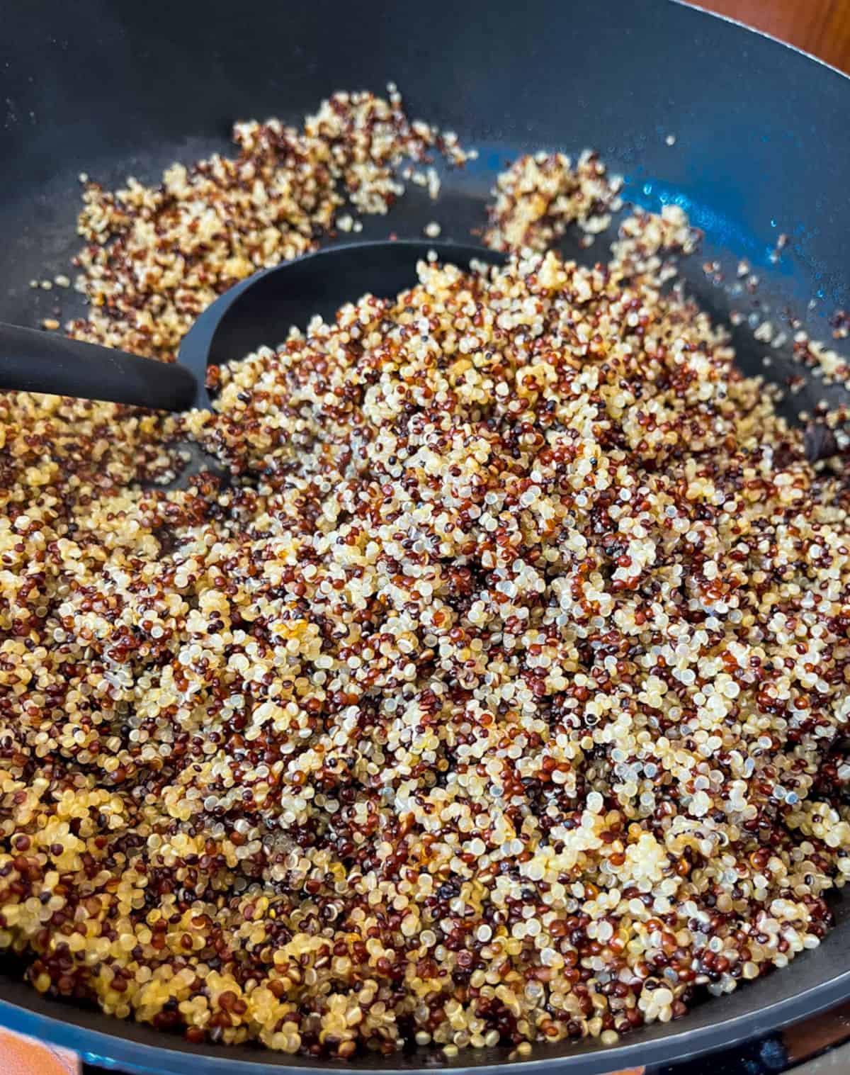 a skillet full of tri-colored quinoa cooked being stirred. by a black spoon