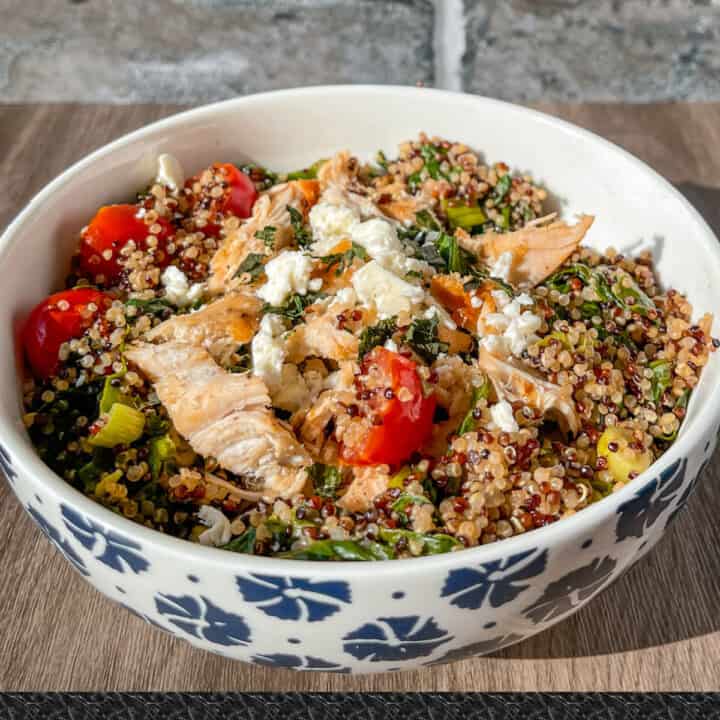 Pesto chicken quinoa bowl in a white bowl with blue painted flowers showcases quinoa mixed with tomatoes, spinach, green onions, feta, chicken, and basil pesto dressing.