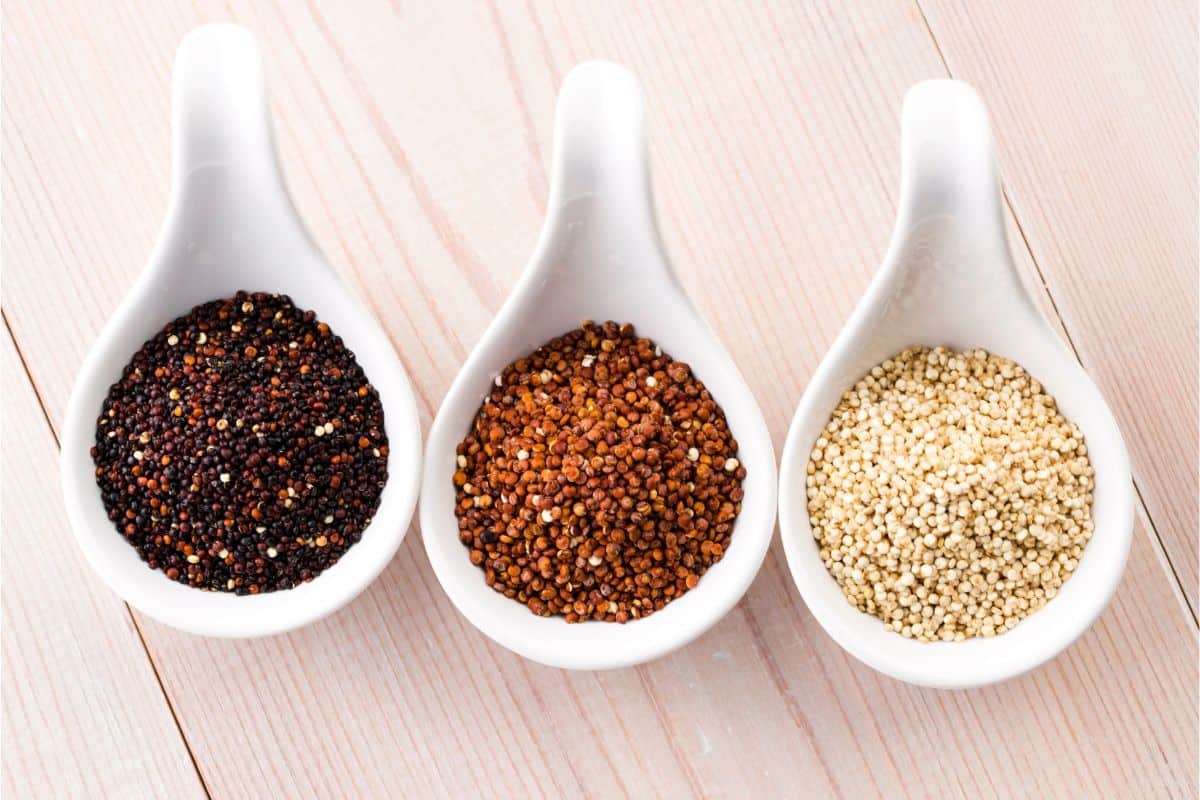 Three decorative white ladles with different types of dry quinoa in them; black, red, and white quinoa.