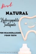 A pinterest formatted photo with blue backdrop has a tip of a white toothpaste tube showing making it appear to have just drawn an outline of a tooth with a smiling face inside of it with toothpaste. The tooth is offset and not showing the whole outline. There is writing in red cursive that reads "BEST" and in black that reads "Natural Hydroxyapatite Toothpaste for Remineralizing Your Teeth". The bottom says mindfullyhealthyliving.com