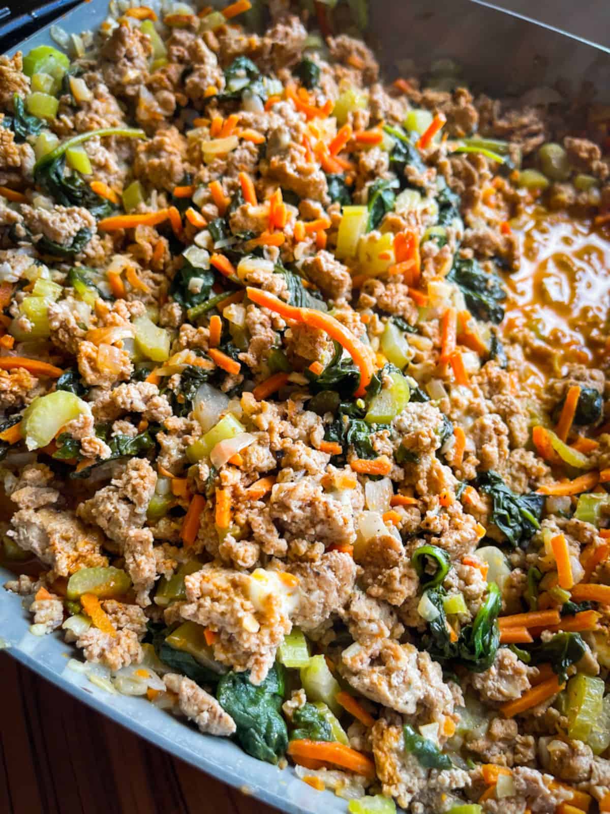 A close up of ground turkey cooked with celery, shredded carrots, garlic, onion, and spinach in buffalo sauce.