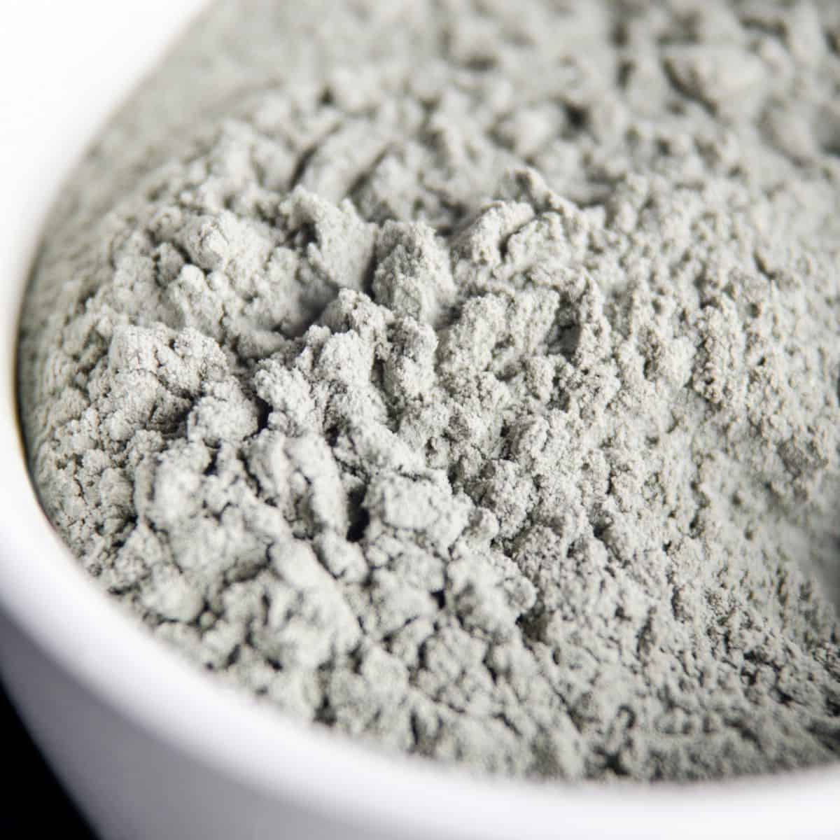 A white bowl of grey-powdered bentonite clay