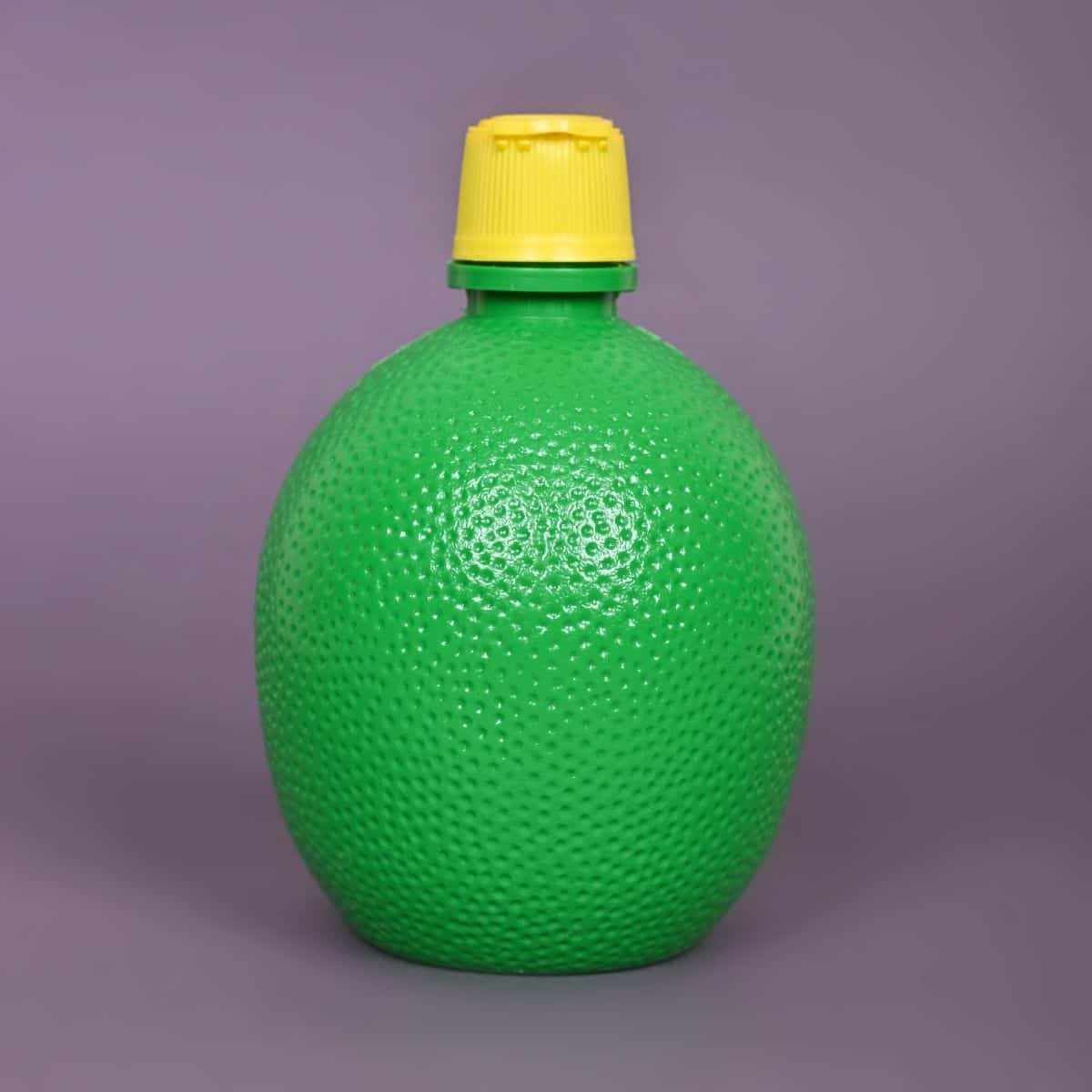 a purple background with a dimpled oval plastic green container of lemon juice concentrate with a yellow lid.