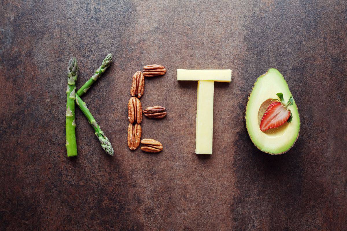 the word keto is spelled out with asparagus, pecans, cheese, and avocado with a strawberry