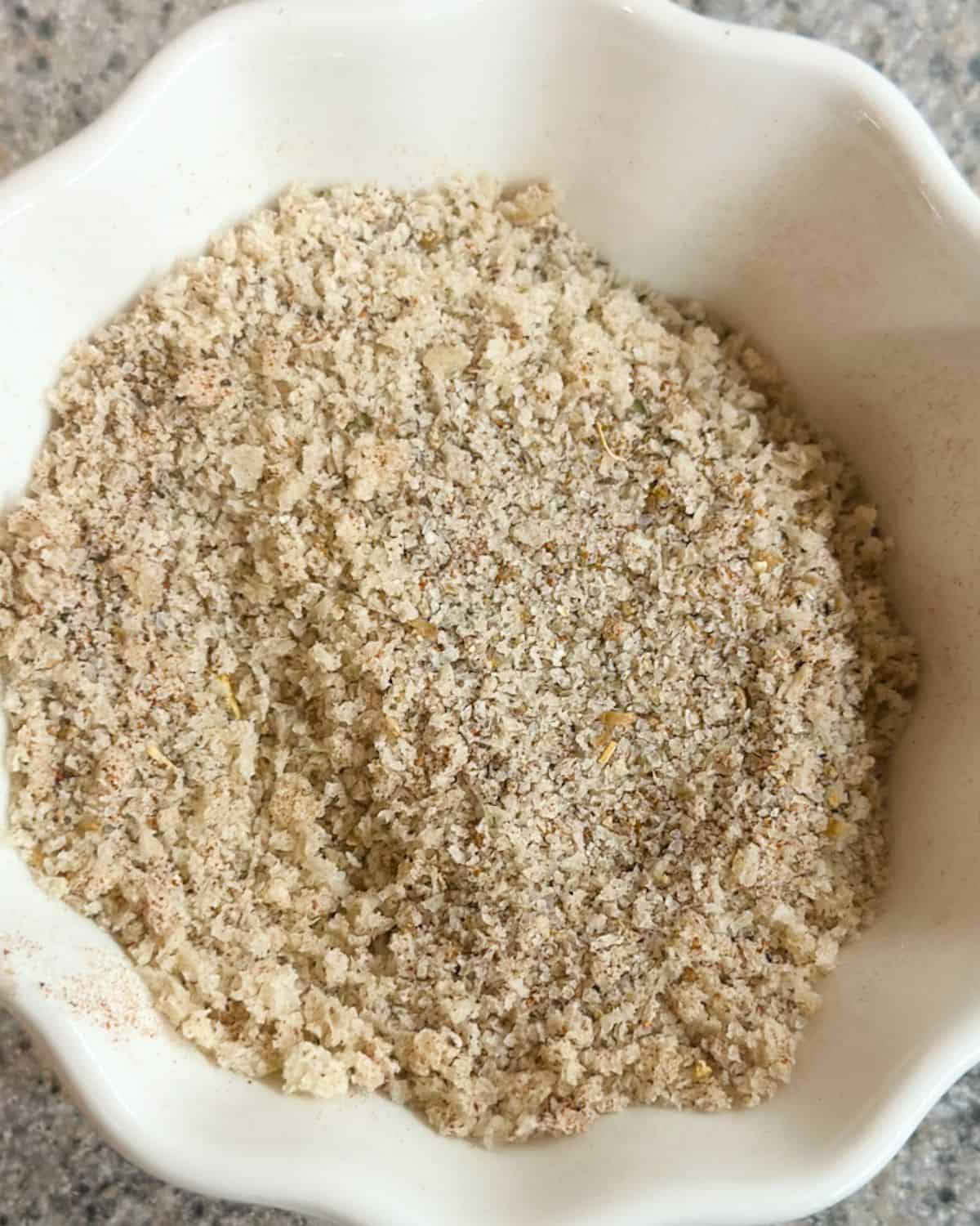 A close up of a white ramekin with panko bread crumbs mixed with seasonings.