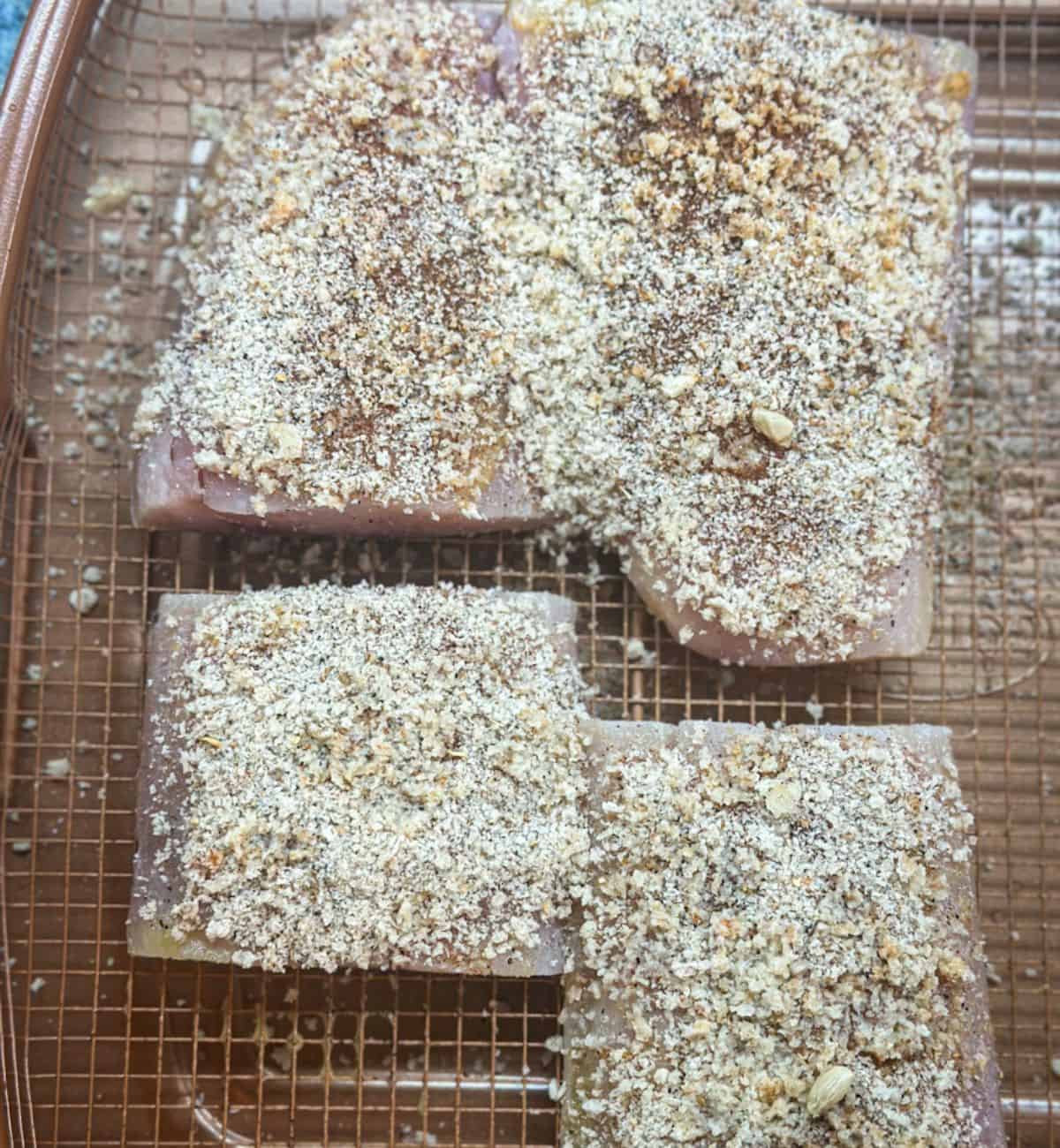 A photo of raw Mahi Mahi fish fillets with bread crumb seasonings on top of them all on an air fryer basket ready to cook.