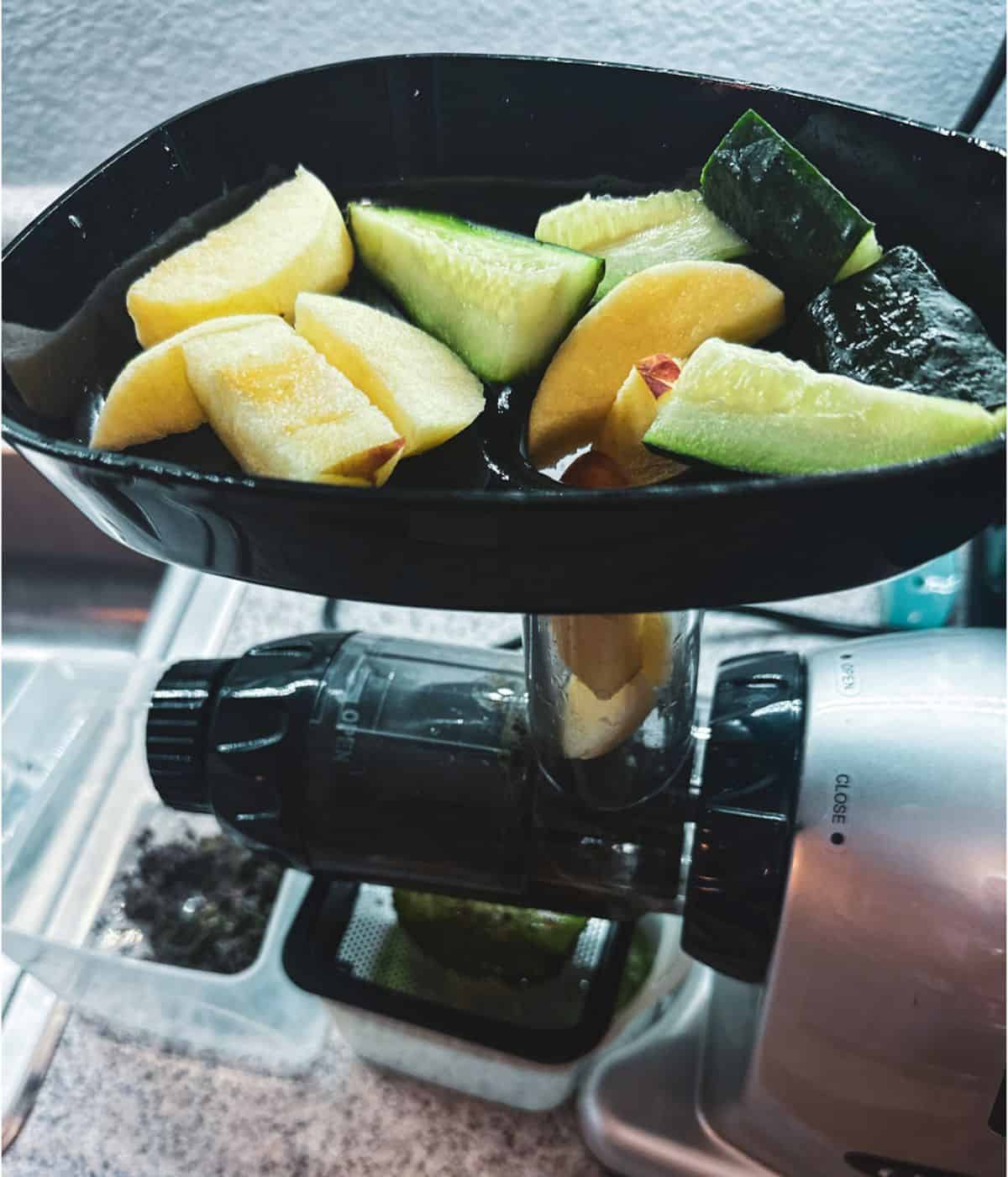 The top view is of a silver and black juicer with apples and cucumbers waiting to be juiced at the top.
