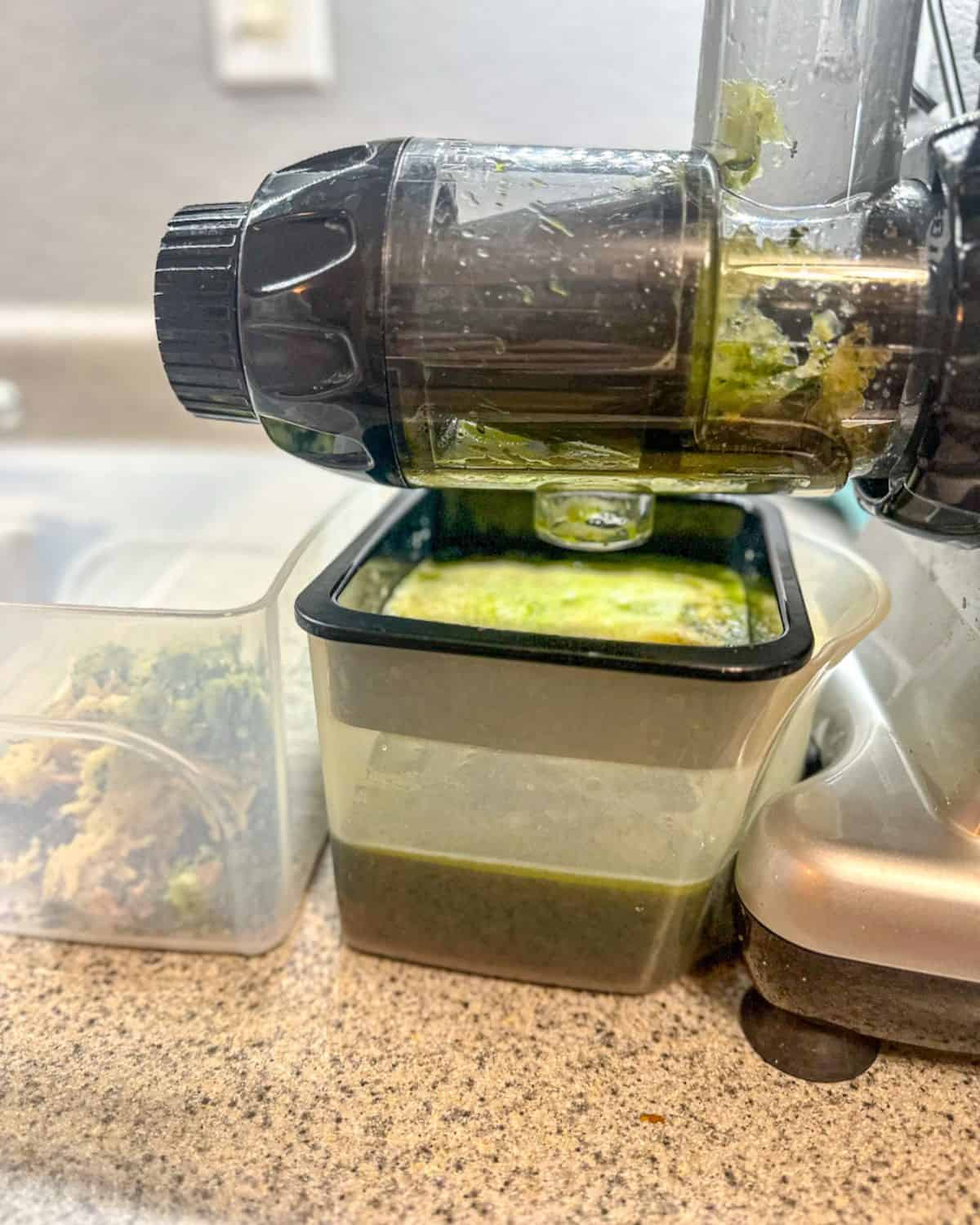 A close-up of the neck and mouth of a juicer with a full container of juice ready to stir and serve. Also visible is the foam in the fine mesh filter and the pulp in the catching container next to the pitcher.