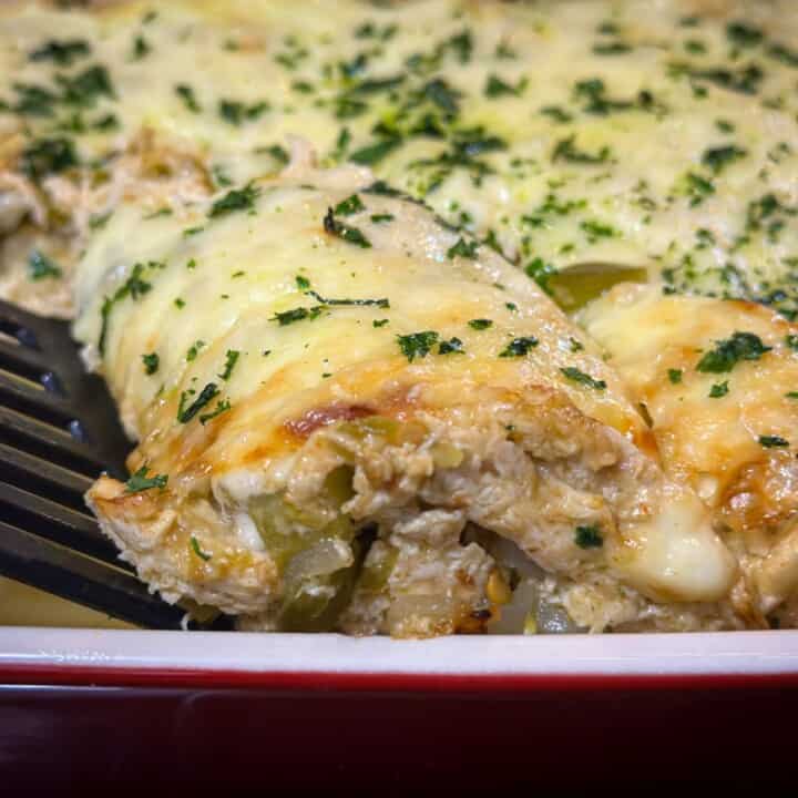 Close-up of a freshly baked casserole with cheese baked on top and chicken, cheese, and green chilies in it as it is being scooped out with a black spatula all in a red and white casserole dish.