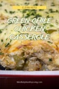 A fill photo of green chile chicken casserole in a red dish with grey dot accents and a yellow box with brown writing at the top that says, Clean Keto. In the middle is a yellow circle drawn with the words green chile chicken casserole in light green writing with a dark green outline. at the bottom says mindfullyhealthyliving.com in white.